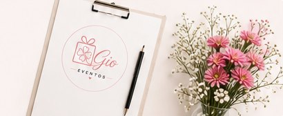 Cuaderno con el logo de By Gio Eventos, lápiz y flores rosadas